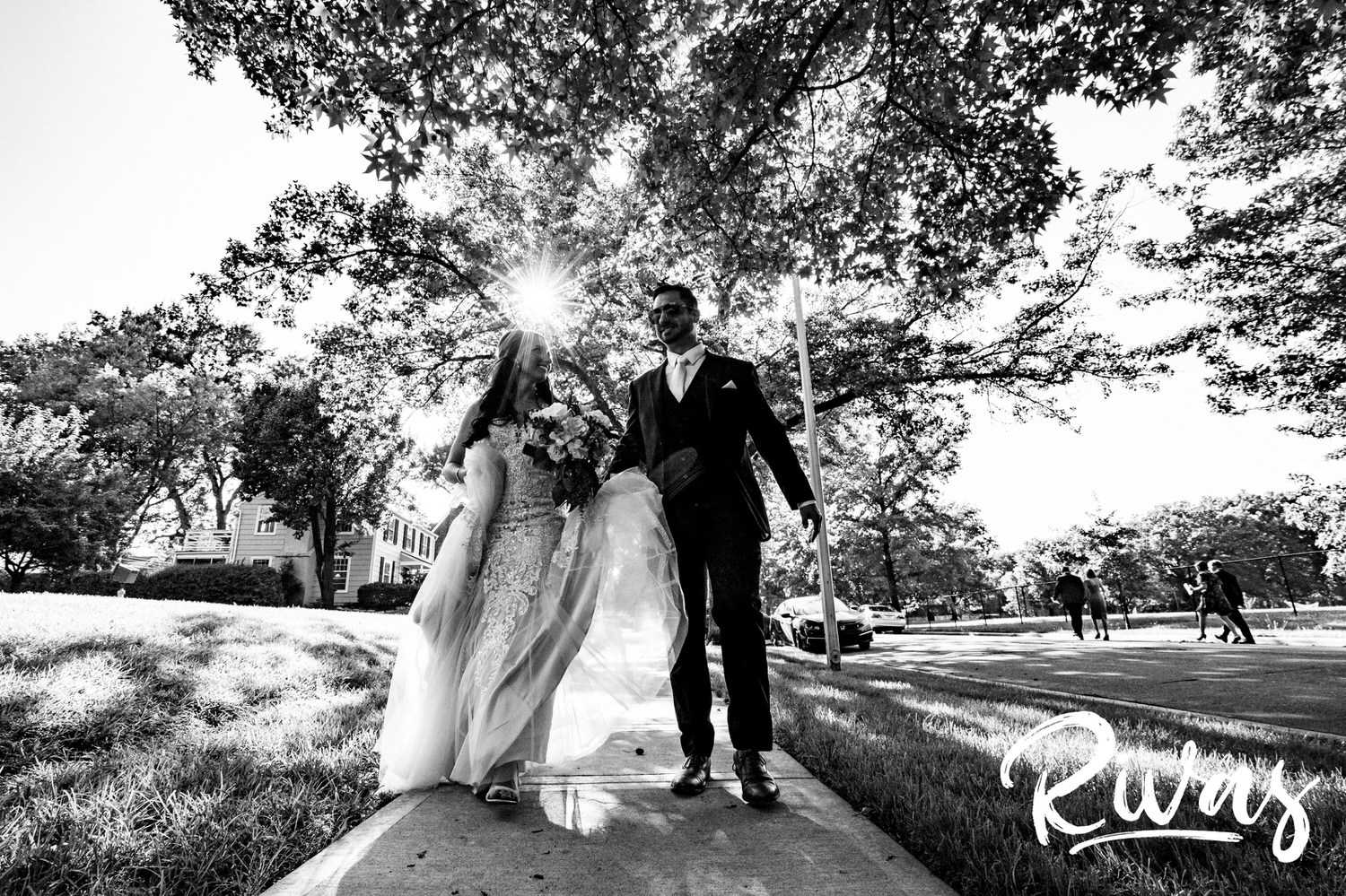 A candid, black and white picture of a bride and groom holding hands, walking down a sidewalk just after their wedding ceremony in Kansas City. 