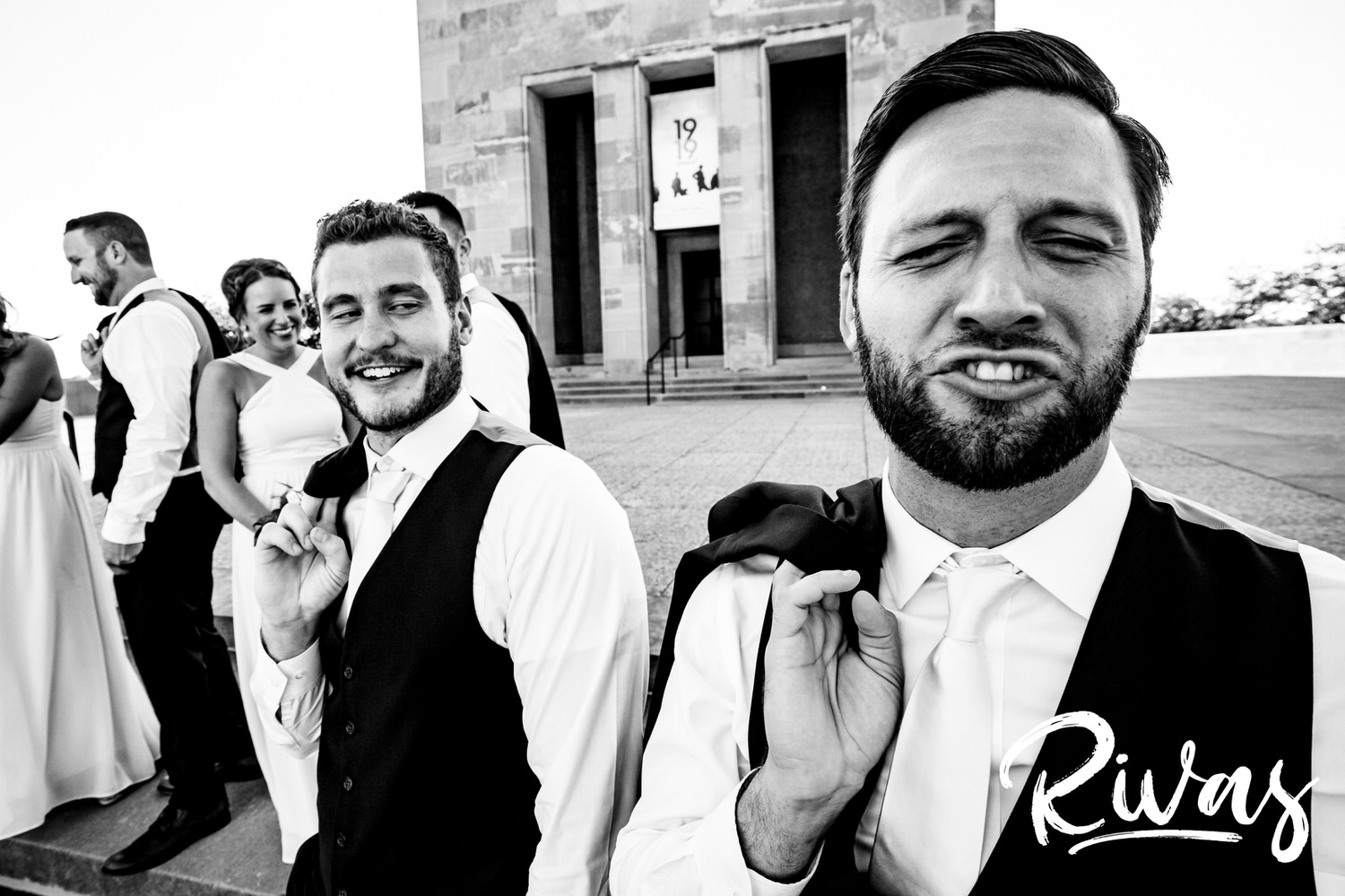A candid, black and white picture of two groomsmen making silly faces at the camera on the afternoon of a wedding day. 