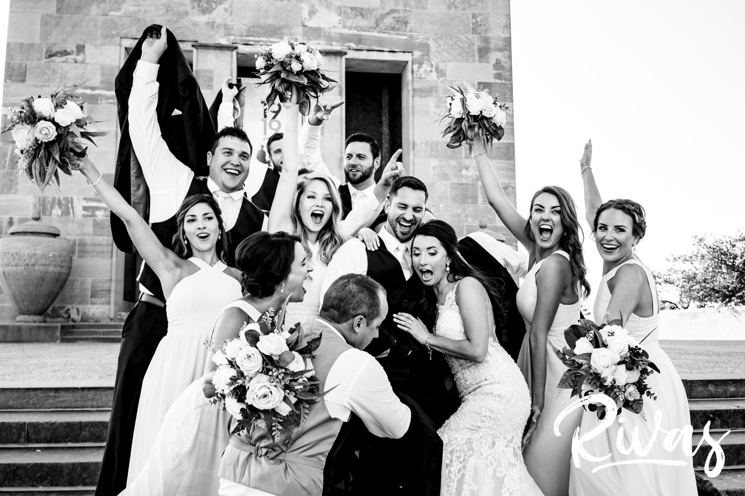 A candid, black and white picture of a wedding party lifting a bride into their air in celebration on a wedding day in downtown Kansas City. 