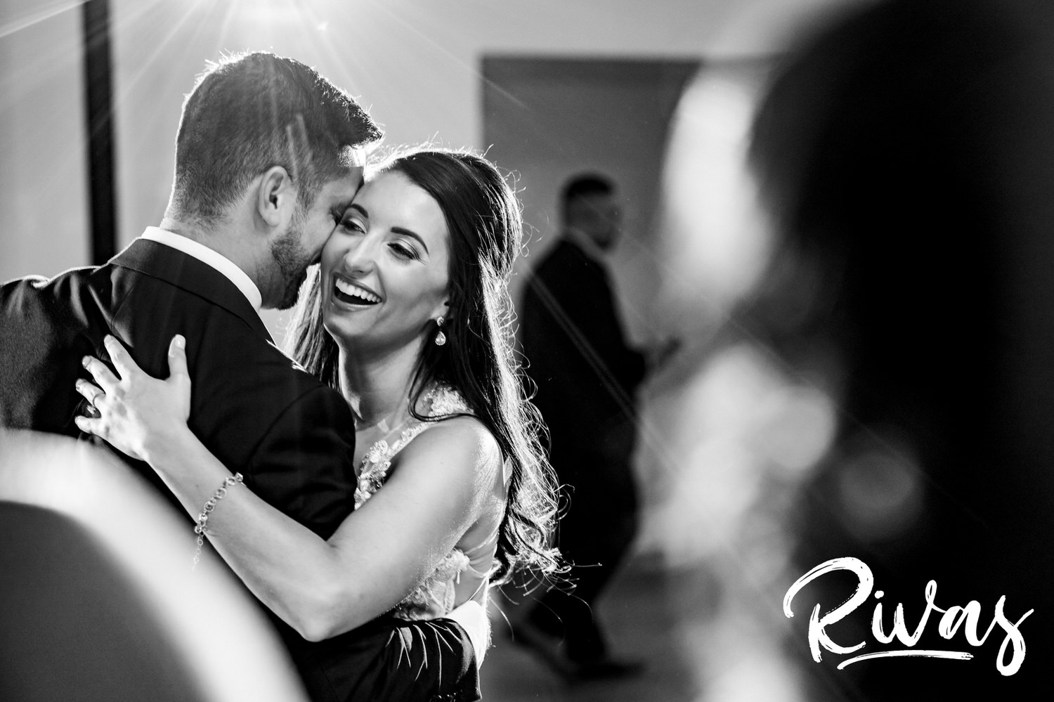 A candid black and white picture of a bride and groom sharing their first dance, as their wedding party stands watching during a wedding reception at The Gallery in downtown Kansas City. 