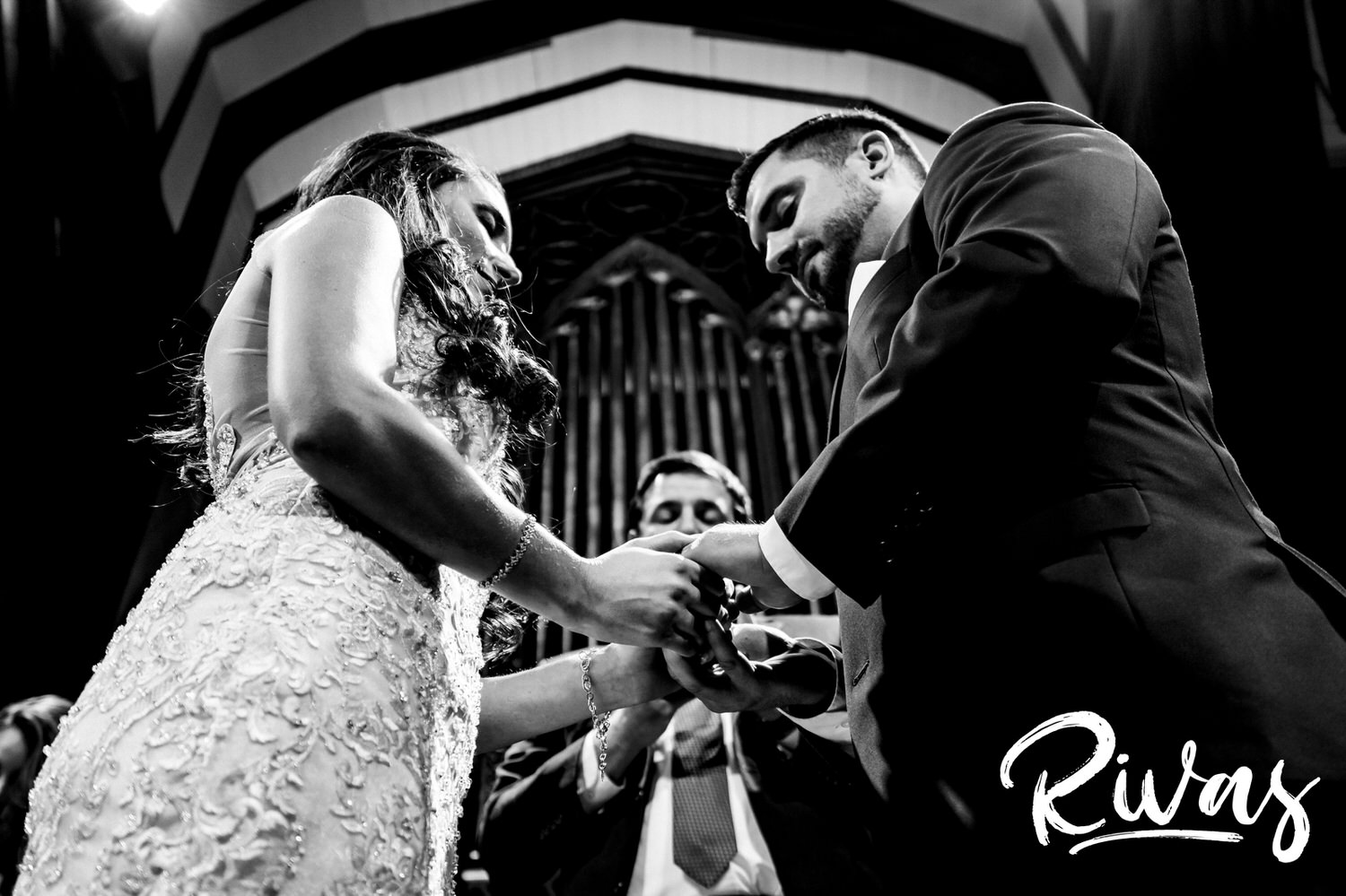 A candid black and white picture of a bride and groom holding hands and exchanging rings during their wedding ceremony in Kansas City. 