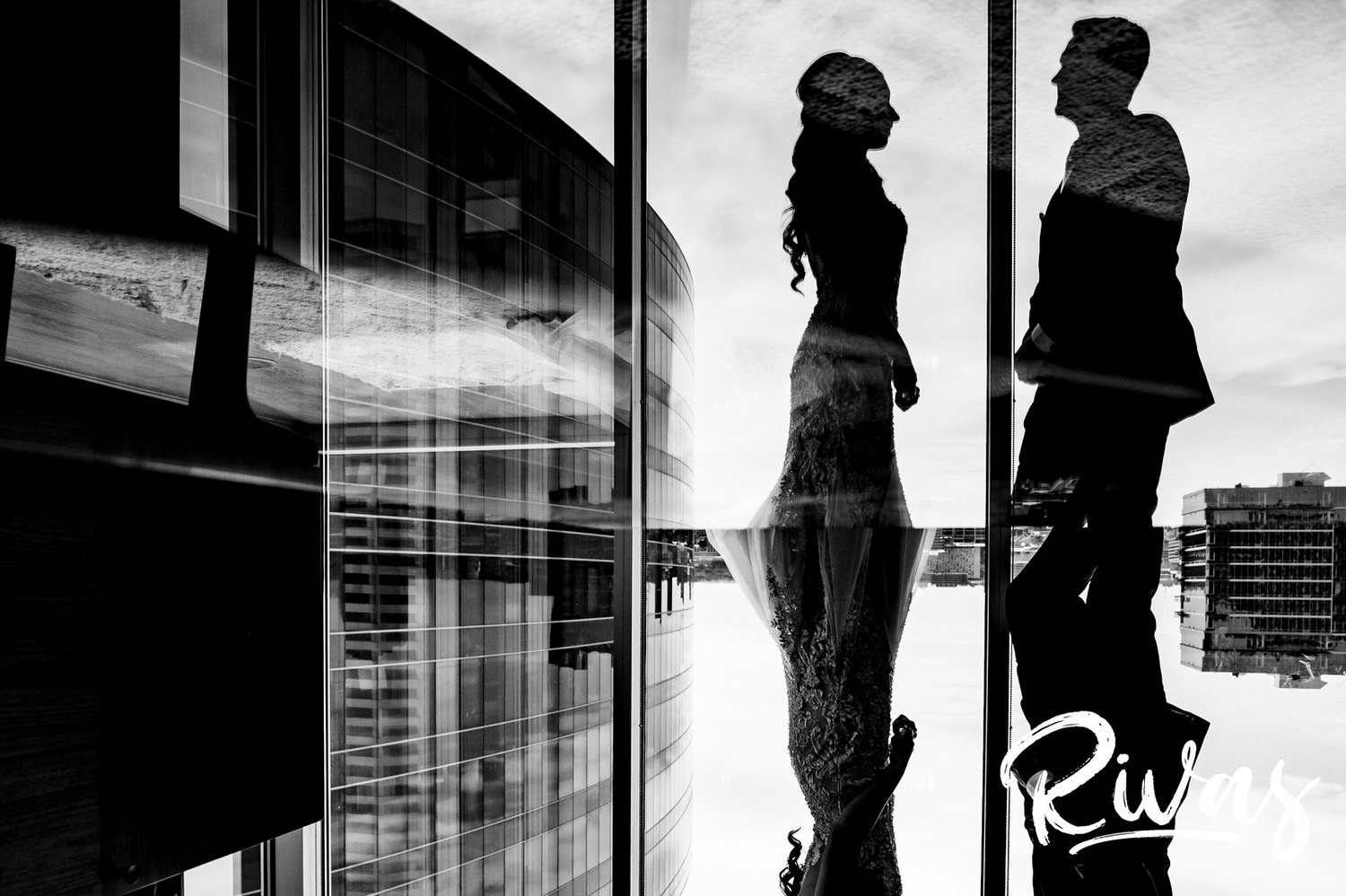 A dramatic, black and white portrait of a bride and groom looking at each other, with their reflections visible below them against the Kansas City skyline on their wedding day. 