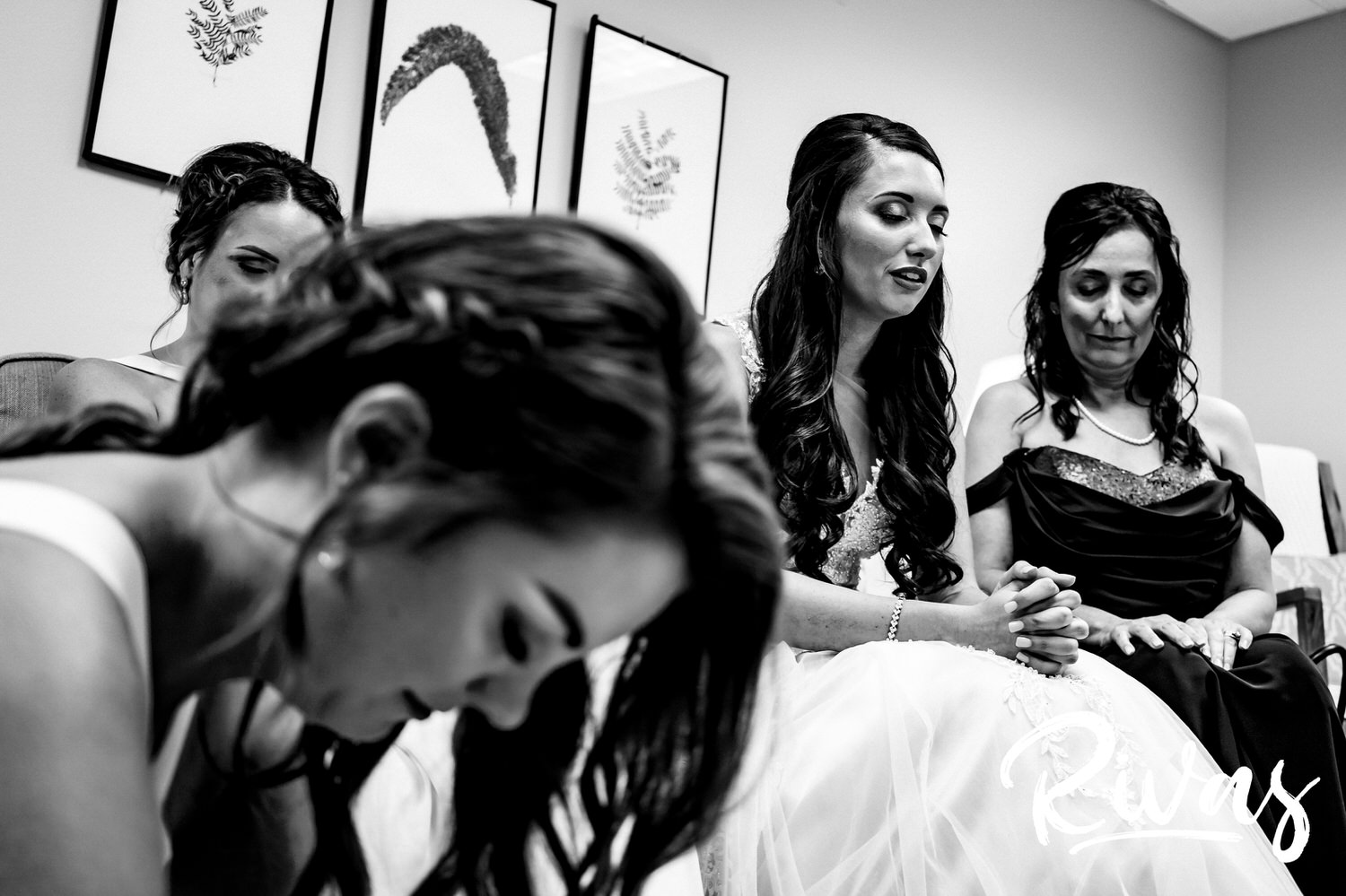 A candid black and white picture taken just before a wedding ceremony of a bride, praying with her bridesmaids and mom.