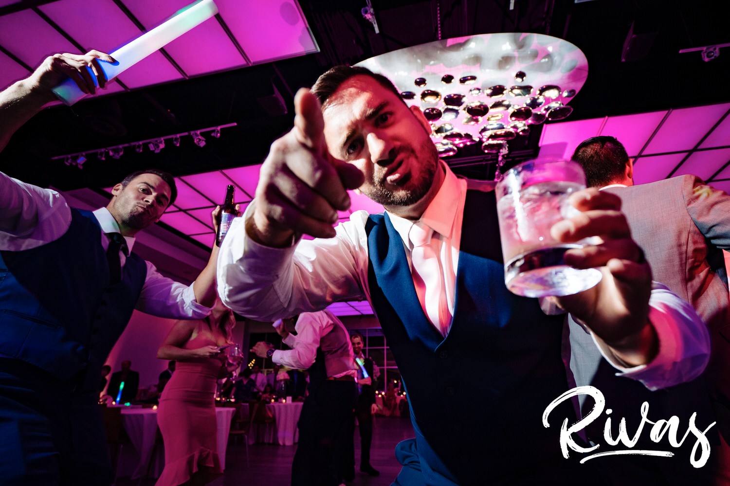 A bright, candid picture of a groom holding a cocktail in one hand and pointing at the camera with the other during his wedding reception in downtown Kansas City at The Gallery Event Space. 