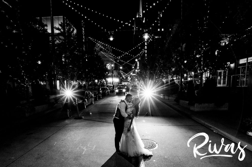 A candid, black and white picture of a bride and groom sharing a kiss in the middle of the street on the night of their wedding in downtown Kansas City.