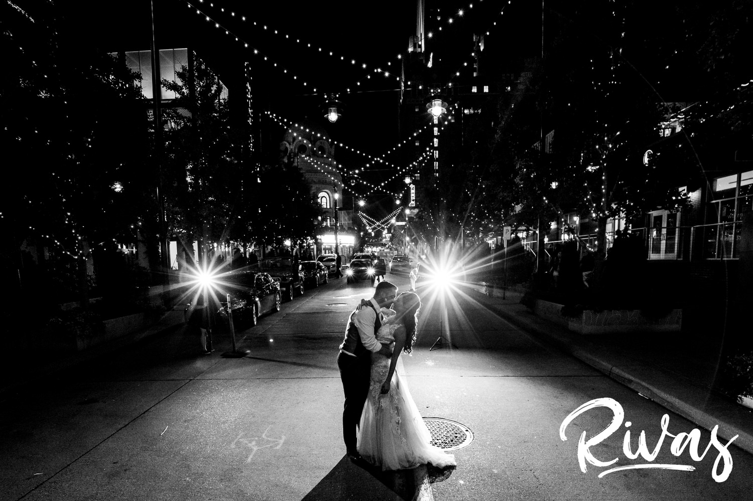 A candid, black and white picture of a bride and groom sharing a kiss in the middle of the street on the night of their wedding in downtown Kansas City. 