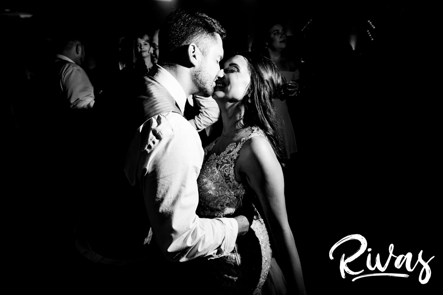 A candid black and white picture sharing a kiss in the middle of a crowded dance floor during their wedding reception at The Gallery Event Space in downtown Kansas City. 