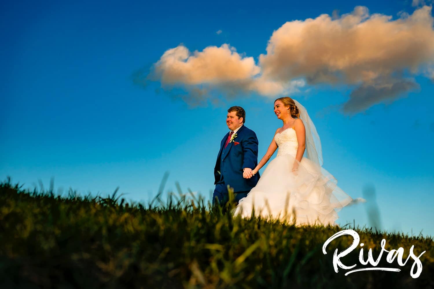 A vibrant, colorful picture of a bride and groom walking hand in hand, smiling and laughing together on their wedding day at Piazza Messina in Cottleville, Missouri. 
