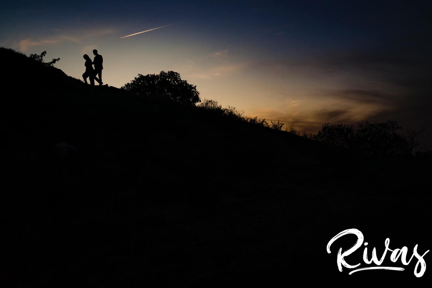 A colorful, silhouetted picture of a man and woman walking together up a hill at the end of their engagement session in Kansas City. 