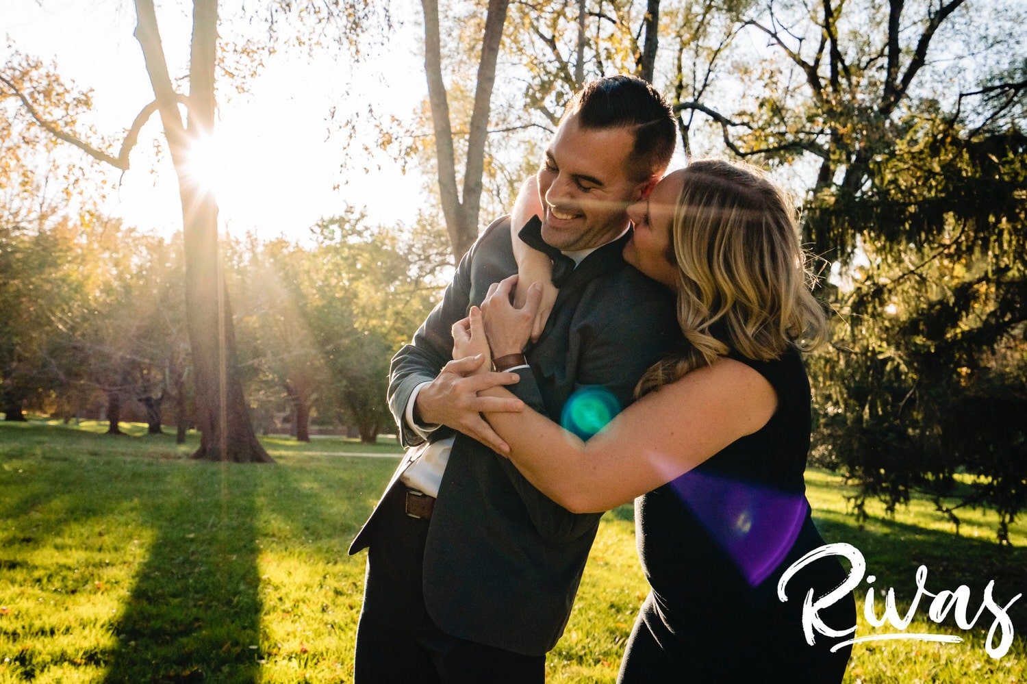 A colorful, candid picture of a woman wrapping her arms around a man in a bow tie and tickling him as they have engagement pictures taken at Kansas City's Loose Park. 