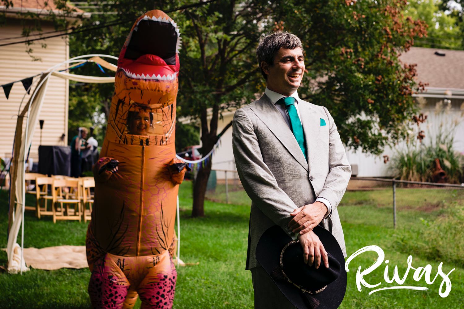 A candid picture of a bride wearing a blow-up t-rex suit approaching her groom wearing a cowboy hat for their first look on their wedding day. 