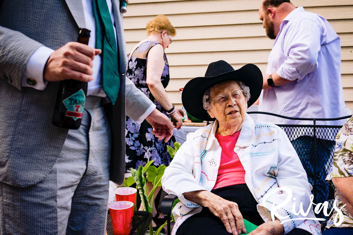 A candid picture of a bride's grandma telling a story as she wears a cowboy hat during an intimate backyard wedding reception in Kansas City. 