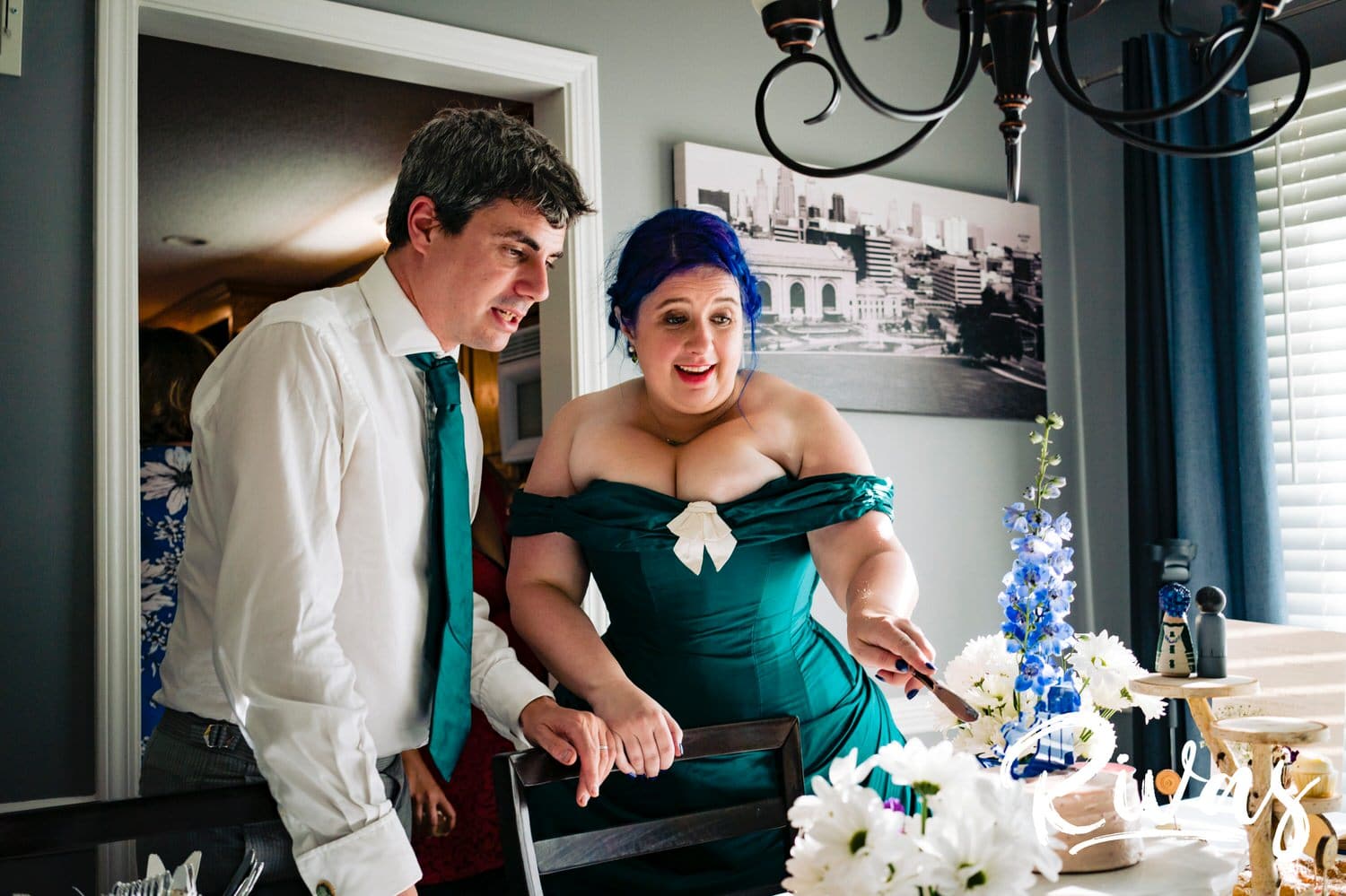 A candid picture of a bride and groom leaning over a dining room table covered in pie, cupcakes, and cake during their intimate backyard wedding reception in Kansas City. 