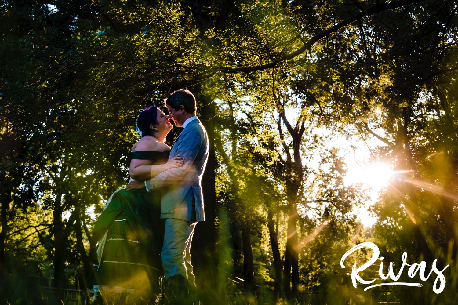 A candid, colorful picture taken during golden hour of a bride in a jade gown and a groom in cowboy boots sharing an embrace as they dance together during their intimate backyard summer wedding reception in Kansas City. 