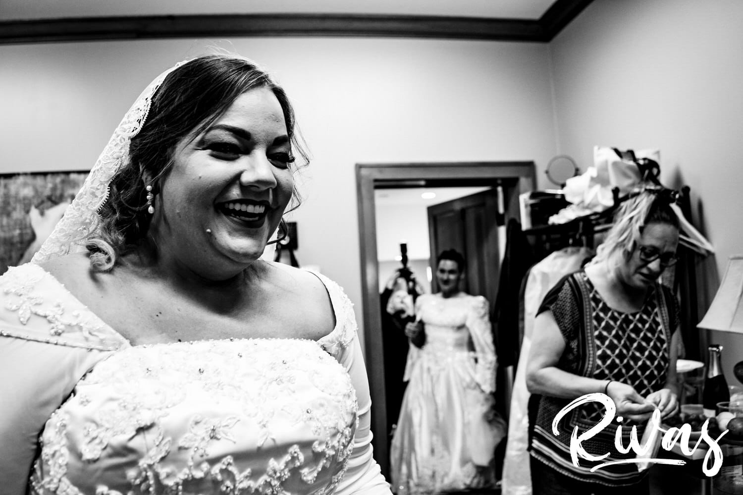 A candid black and white picture of a bride laughing as her brother in law comes out of the bathroom also wearing a wedding dress. 