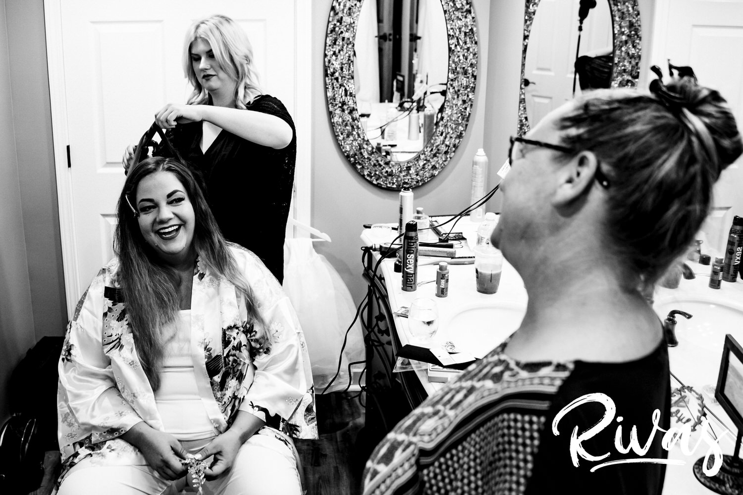 A candid black and white picture of a bride's aunt smiling in at her as she gets her hair and make-up done on the morning of her wedding at Fire Stables. 