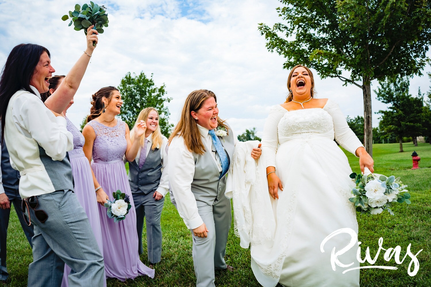 A candid picture of two brides and their wedding party laughing hysterically on their wedding day at Fire Stables. 