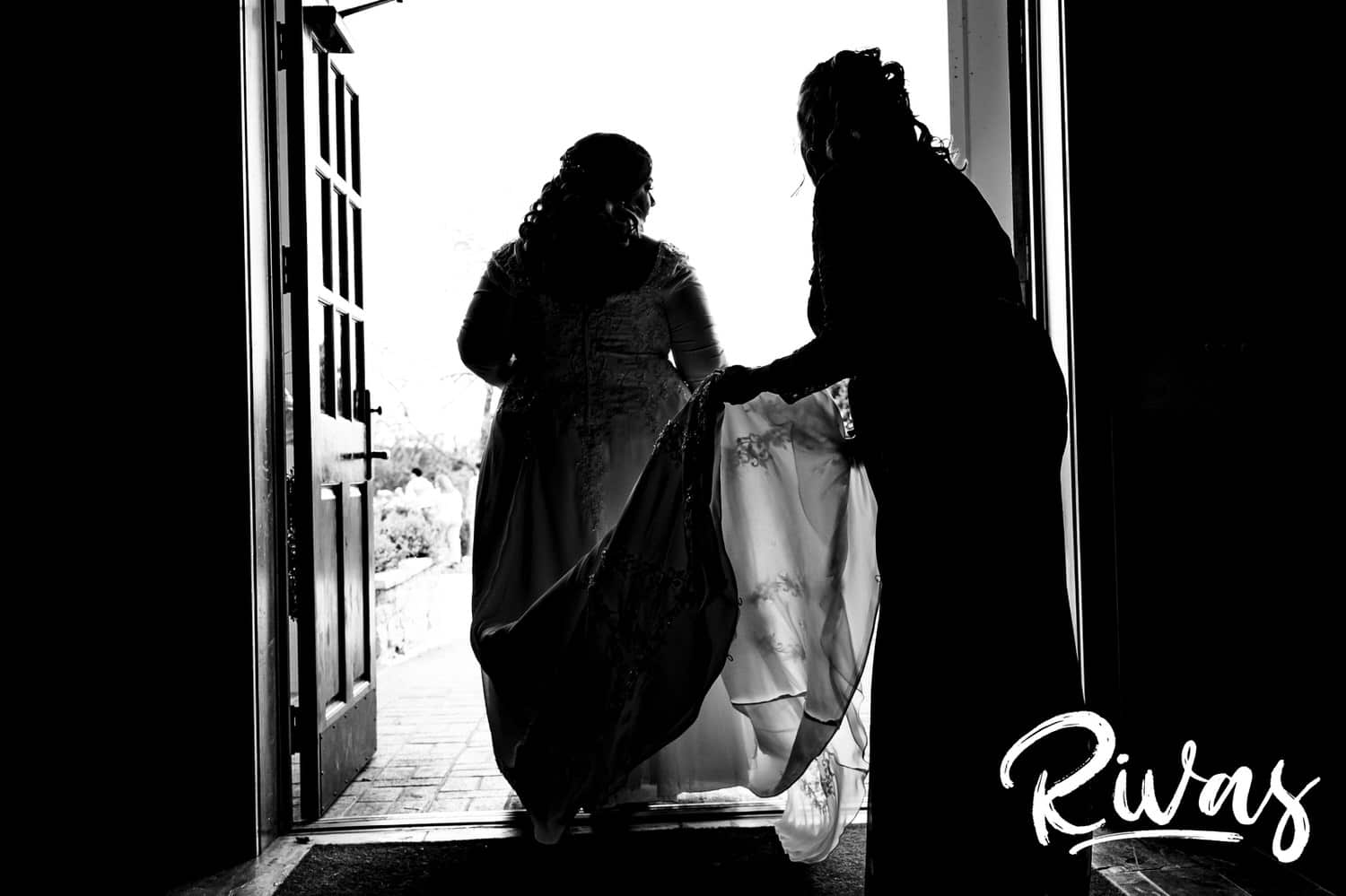 A candid black and white picture of a bride's mom holding her skirt up as she walks out the door of Fire Stables to get married. 