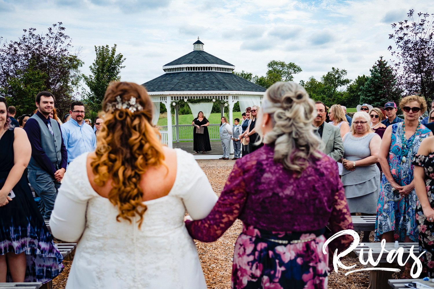 A candid, colorful picture of a bride walking down the aisle with her mom, with her bride in her line of sight. 