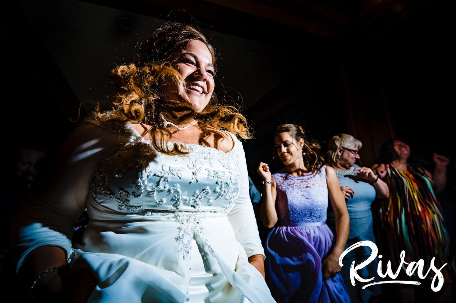 A candid picture of a bride jumping around with her sister and reception attendees during her Fire Stables wedding reception. 