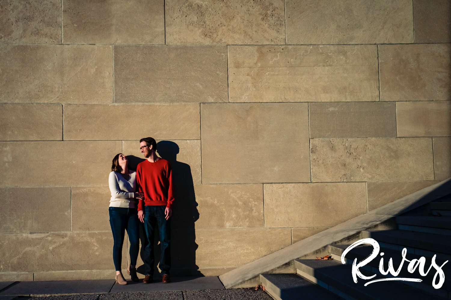 A candid picture of an engaged couple sharing an embrace and leaning up against a stone wall at Liberty Memorial during their fall engagement session in Kansas city. 