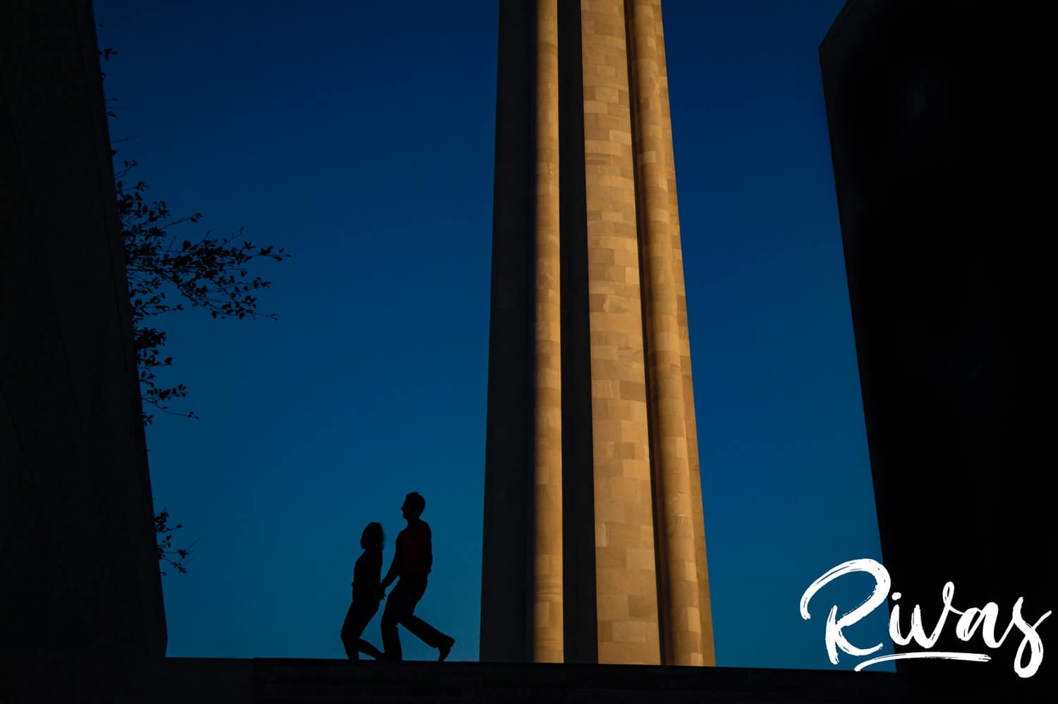 A silhouetted image of an engaged couple holding hands and walking across the top of the stairs at Liberty Memorial taking engagement photos. 