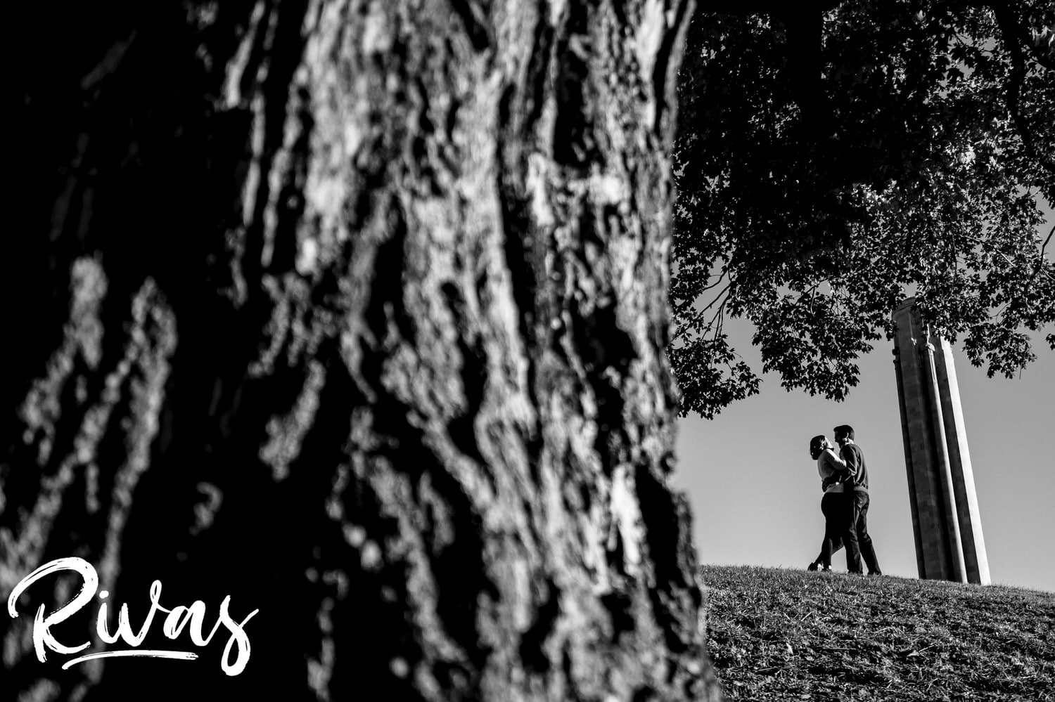 A distant, black and white portrait of an engaged couple standing on a hill in front of Liberty Memorial during their KC engagement session. 