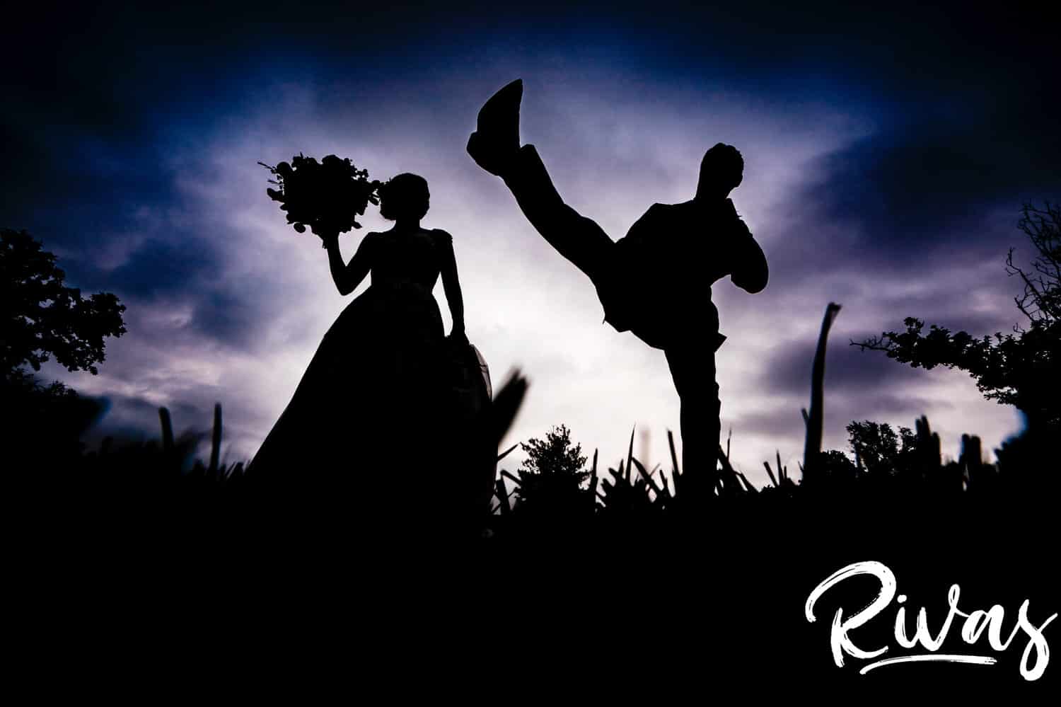 A silhouetted picture of a groom kicking his leg high into the air as his bride watches on their wedding day at The Bowery Event Space.