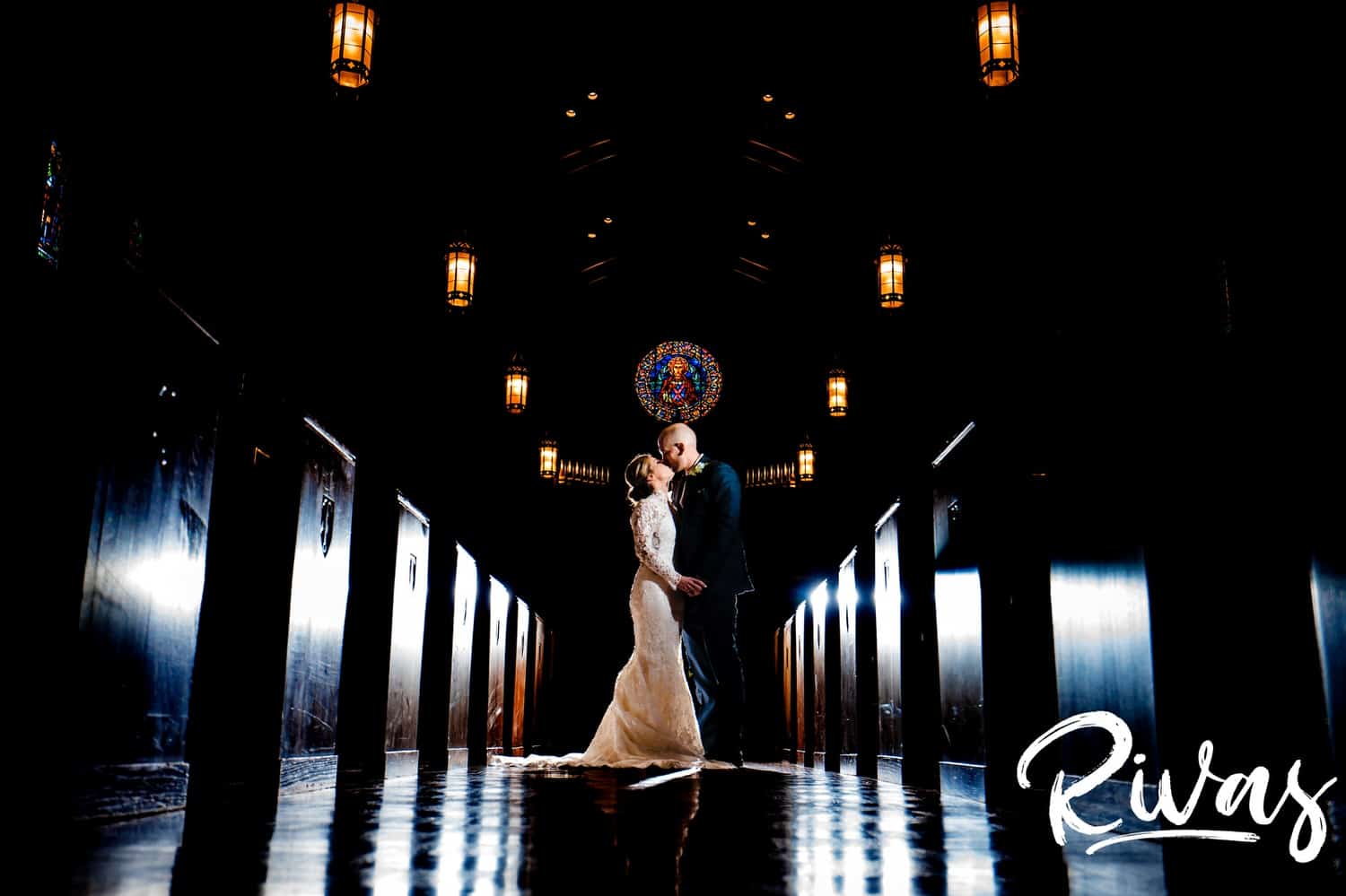 A dramatic portrait of a bride and groom standing in the middle of a church aisle, sharing a kiss moments before their winter wedding begins in Kansas City. 