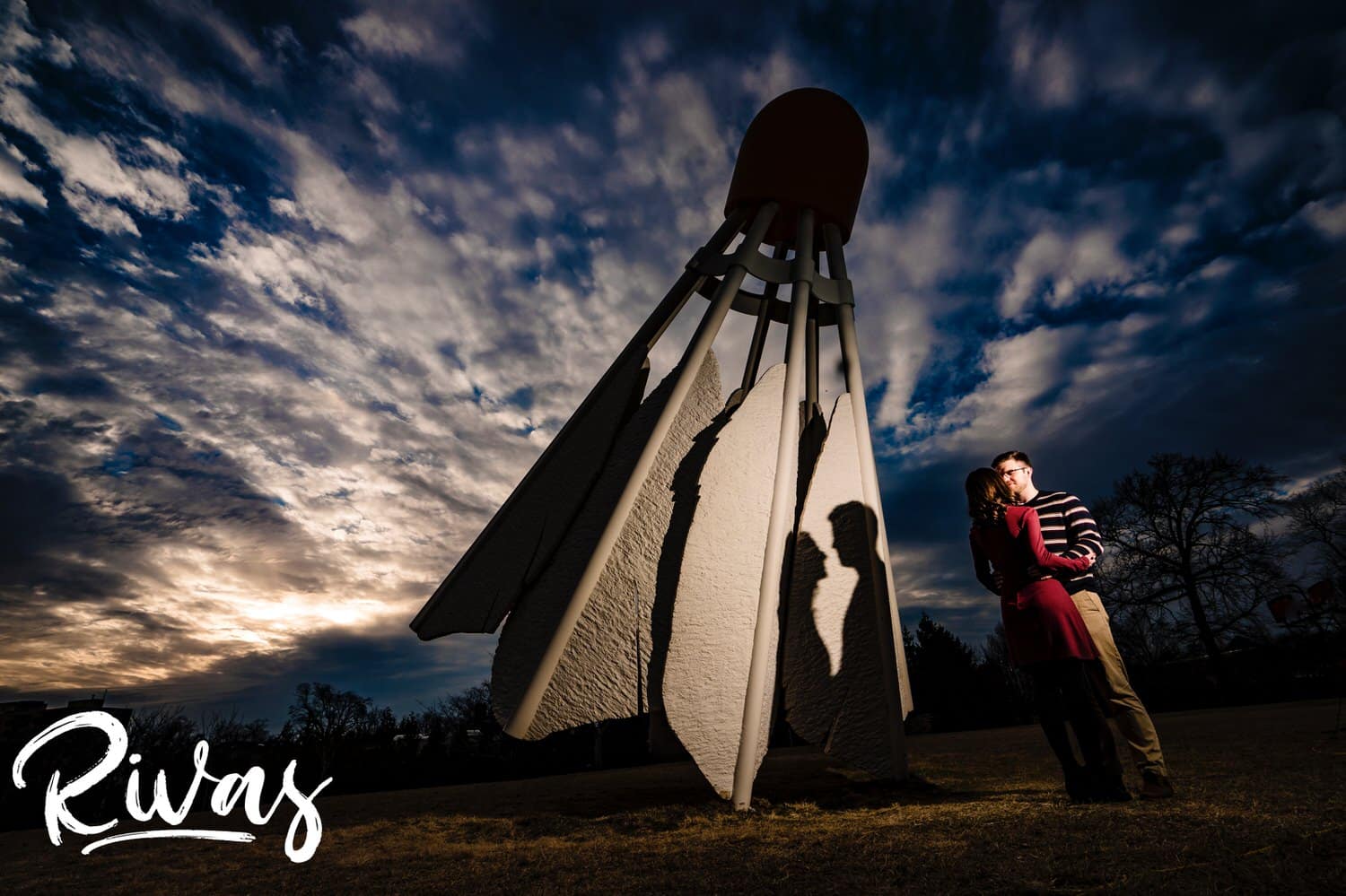 A dramatic portrait of an engaged couple sharing an embrace in front of an iconic shuttlecock on the lawn of the Nelson Atkins Museum of Art in Kansas City. 