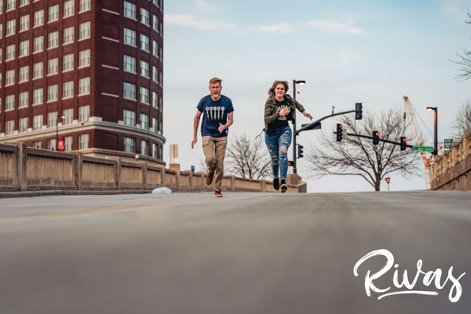 A candid picture taken from a distance of a man and woman sprinting towards the camera in downtown Kansas City during their winter engagement session.. 
