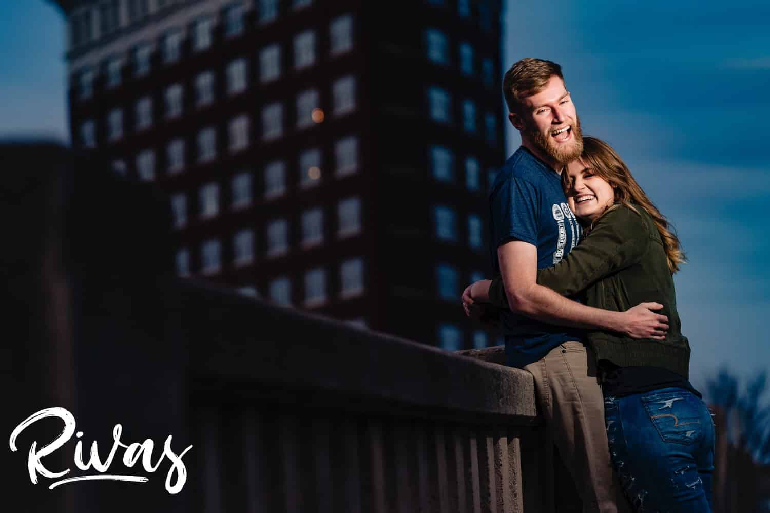 A candid portrait of an engaged couple sharing an embrace in front of the Western Auto Building during their downtown Kansas City engagement session. 