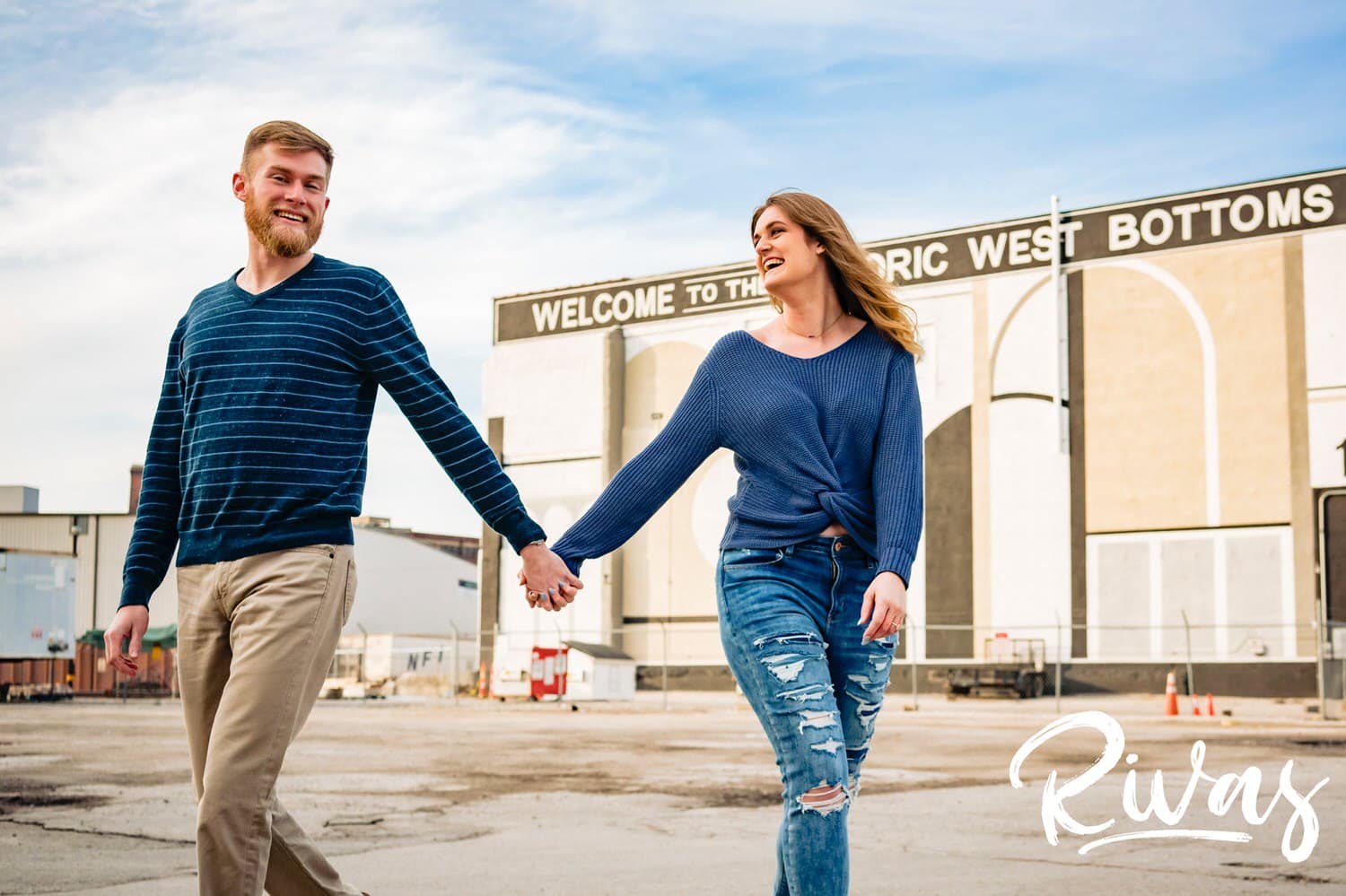 A candid picture of an engaged couple holding hands and laughing together as they walk down the middle of the street during their West Bottoms Engagement Session in Kansas City. 