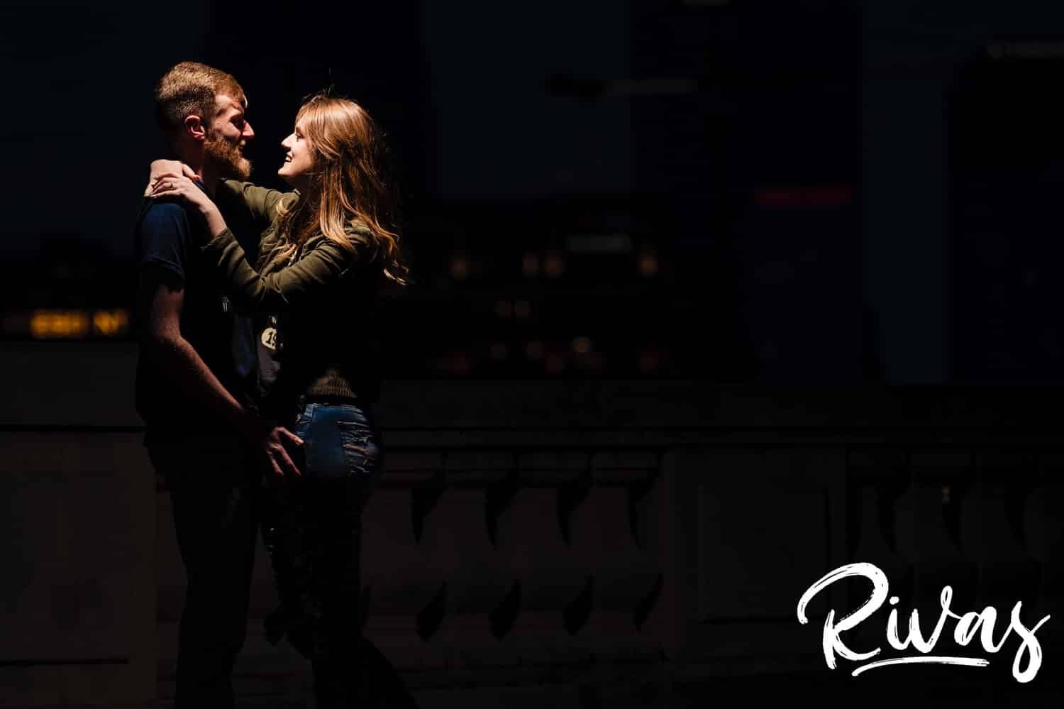 A candid, bold picture of an engaged couple spotlit from above leaning in to share a kiss during their winter engagement session in downtown Kansas City. 