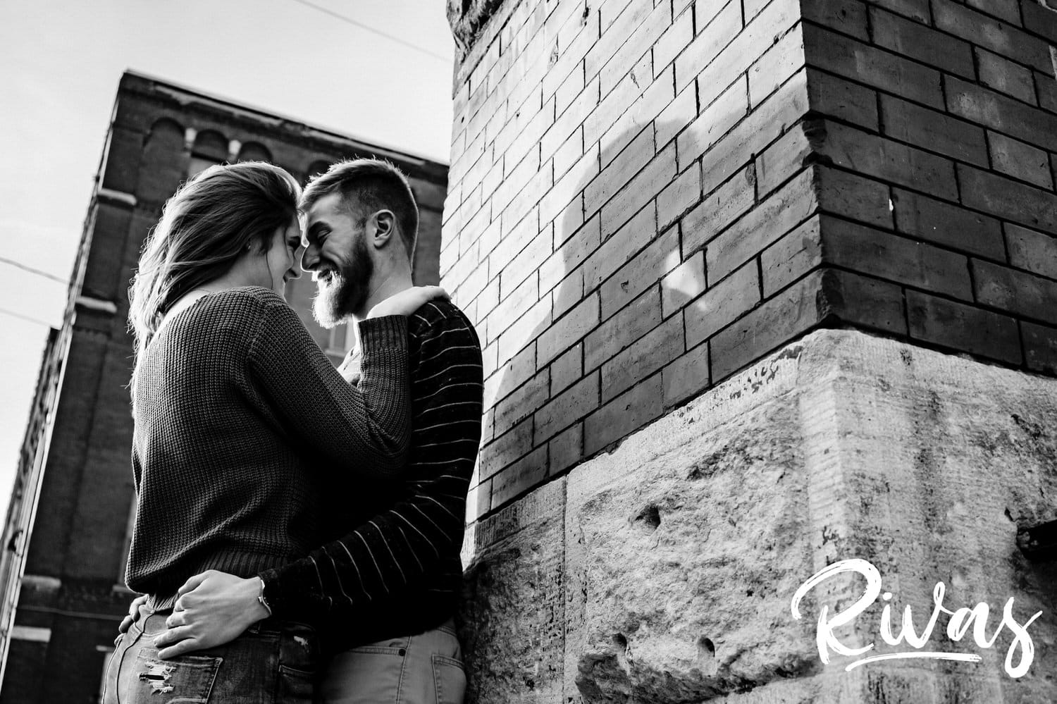 A close-up picture of an engaged couple leaning in for a kiss as they lean up against a brick wall during their engagement session in Kansas City's West Bottoms neighborhood. 