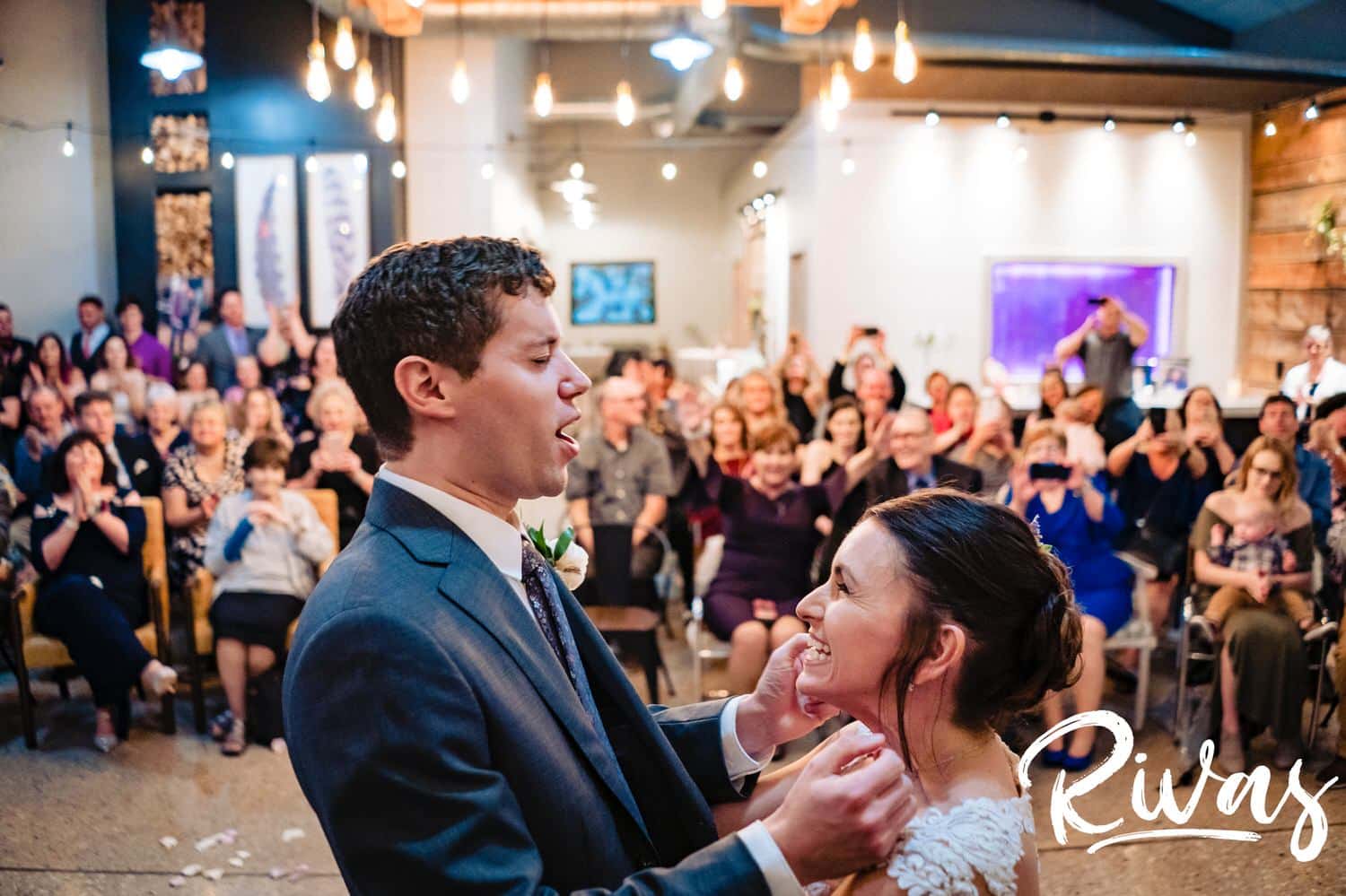 A colorful, celebratory picture of a bride and groom excitedly holding hands and yelling  just after their first kiss at the end of their wedding ceremony at The Bowery in Kansas City. 