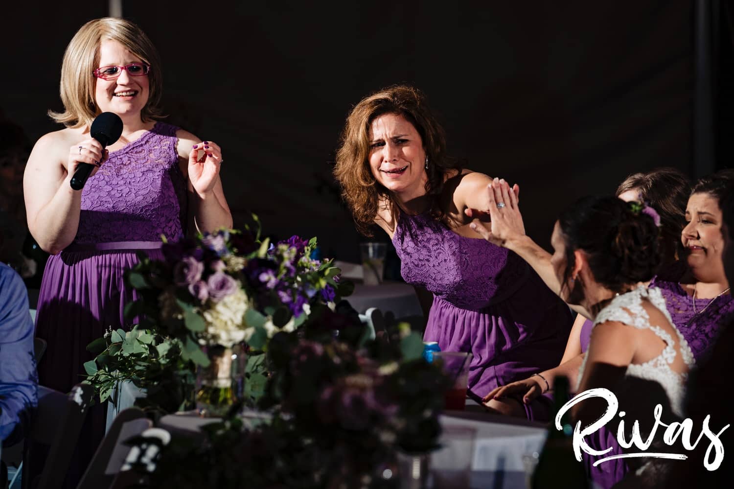 A colorful, candid picture of a bride high-fiving her bridesmaid as she toasts her during a rainy wedding reception at The Bowery in Kansas City. 