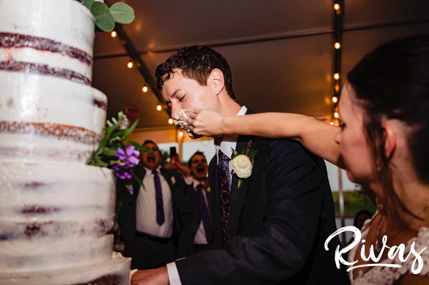 A colorful, candid picture of a bride and groom cutting their wedding cake during their tented reception at The Bowery in Kansas City. 