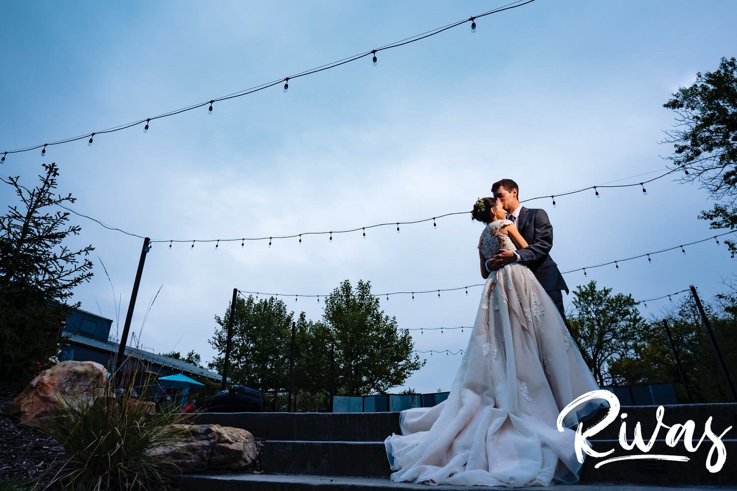 A dramatic portrait of a bride and groom sharing an embrace on a set of stairs on the afternoon of their rainy wedding day at The Bowery in Kansas City. 