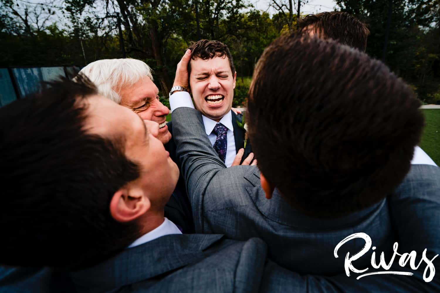 A close-up, candid picture of a groom reacting as his groomsmen pull him in for a group hug on the afternoon of his wedding day at The Bowery in Kansas City. 