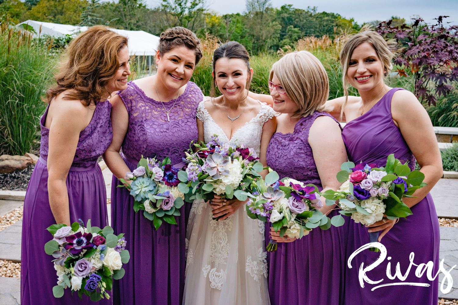 A colorful, candid picture of a bride and her bridesmaids, all dressed in purple laughing together on a rainy afternoon at The Bowery in Kansas City. 