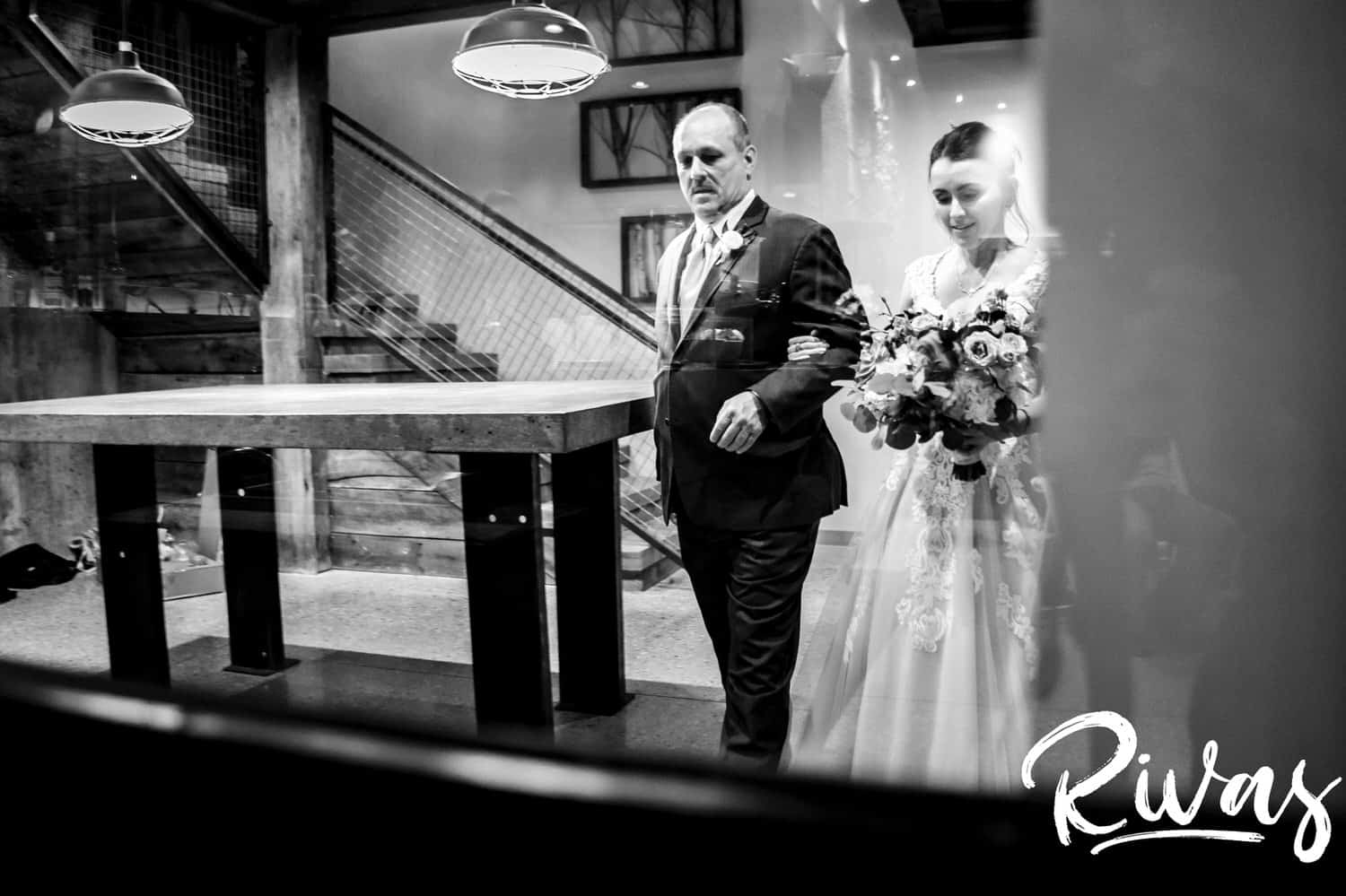 A candid, black and white picture of a bride and her father rounding a corner getting ready to walk down the aisle on her rainy wedding day at The Bowery in Kansas City. 
