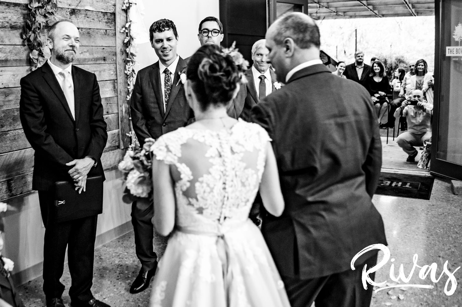 A candid black and white picture taken of a bride and her father as they approach her groom and officiate on the afternoon of a rainy ewdding ceremony at The Bowery in Spring Hill. 
