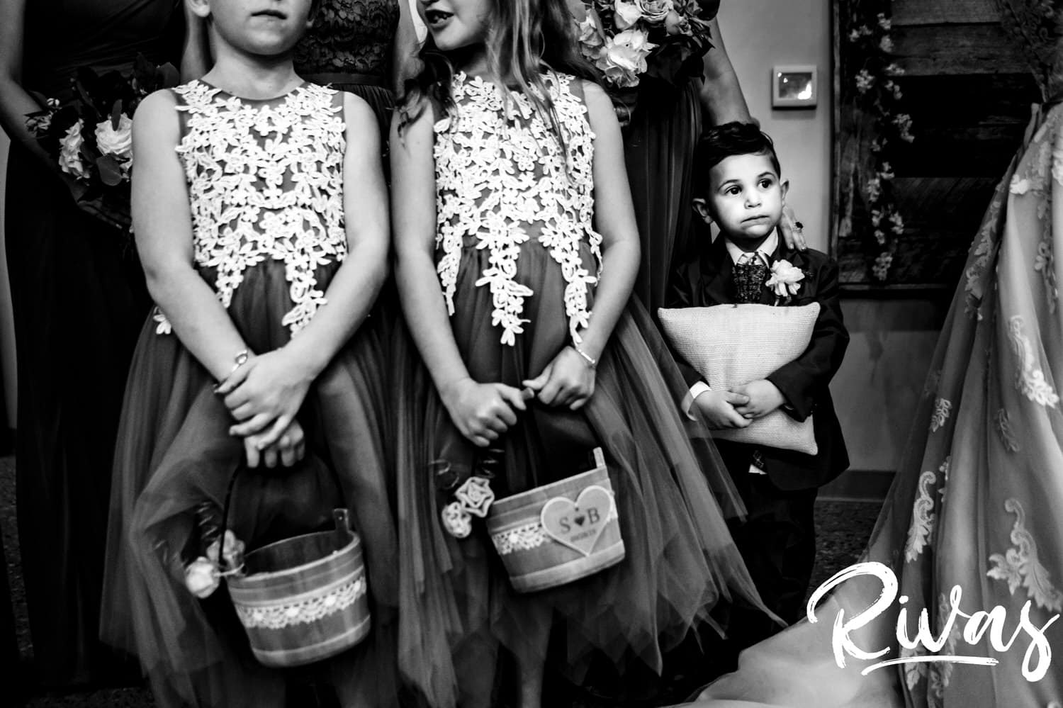 A candid black and white picture of a ring bearer hugging his pillow tightly to his chest as his sisters, the flowergirls, hold their flower buckets during a wedding ceremony at The Bowery in Kansas City. 