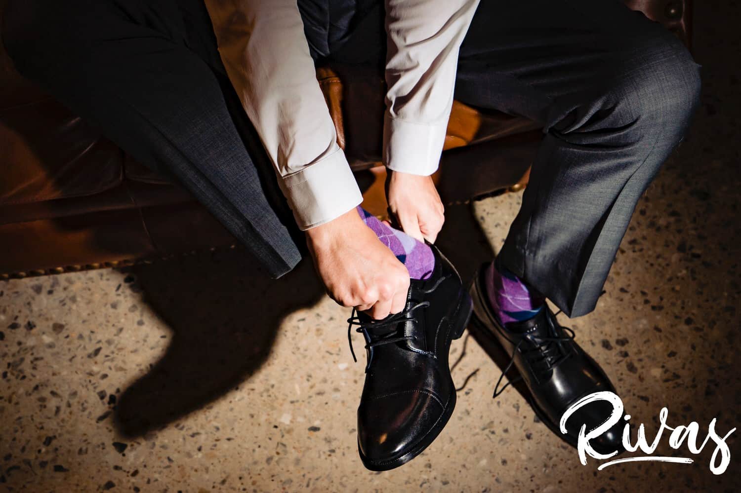 A candid, close-up picture of a man putting dress shoes on over his purple plaid socks on the morning of his rainy wedding day at The Bower just outside Kansas City. 