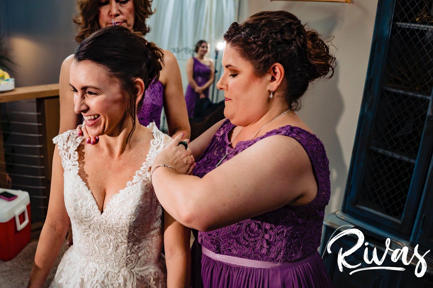 A colorful, candid picture of a bridesmaid zipping up the back of a bride's gown on the morning of her wedding at The Bowery in Kansas City. 