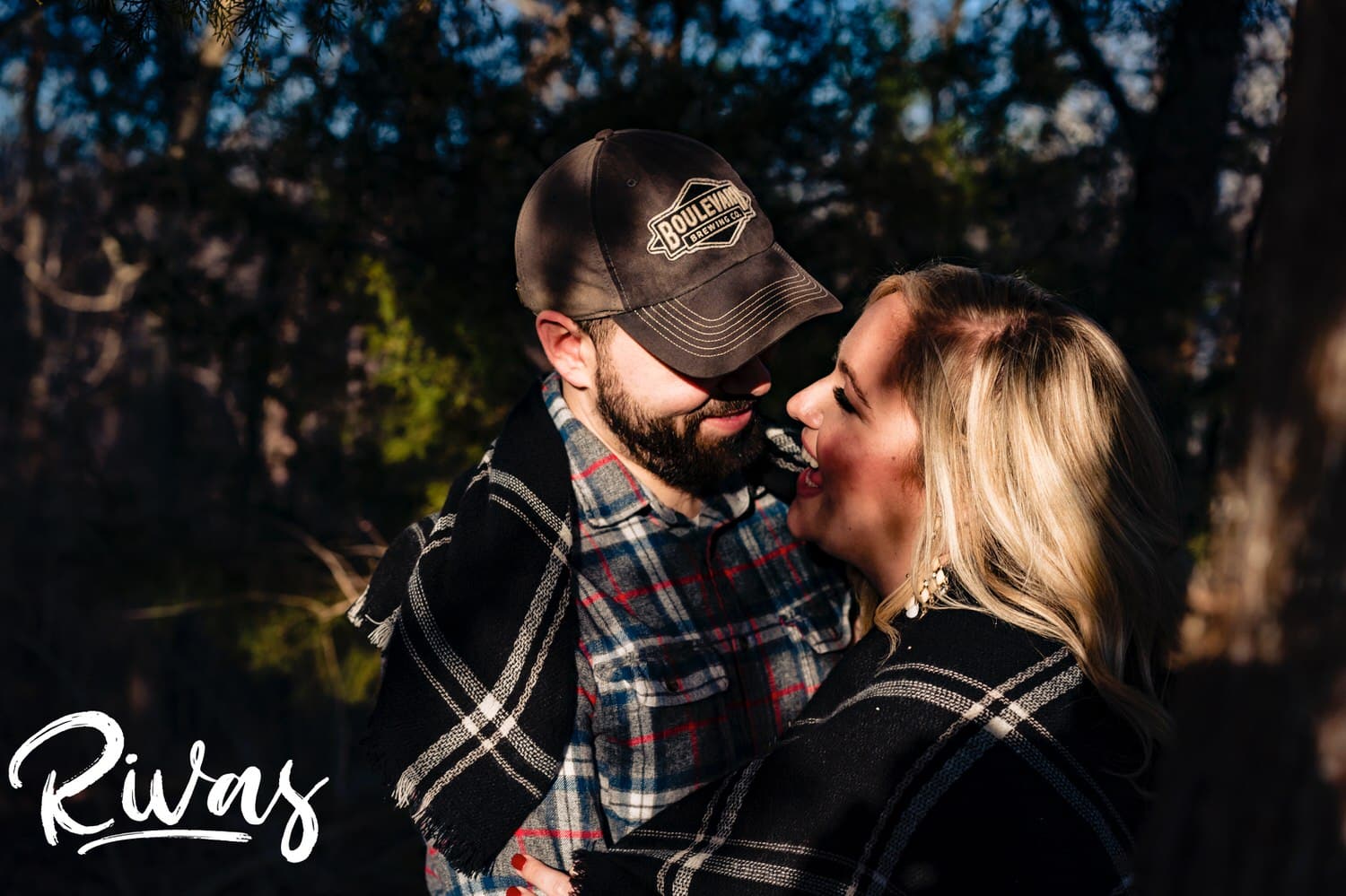 A candid picture taken through a tree of an engaged couple sharing an embrace and kiss during their winter engagement session. 