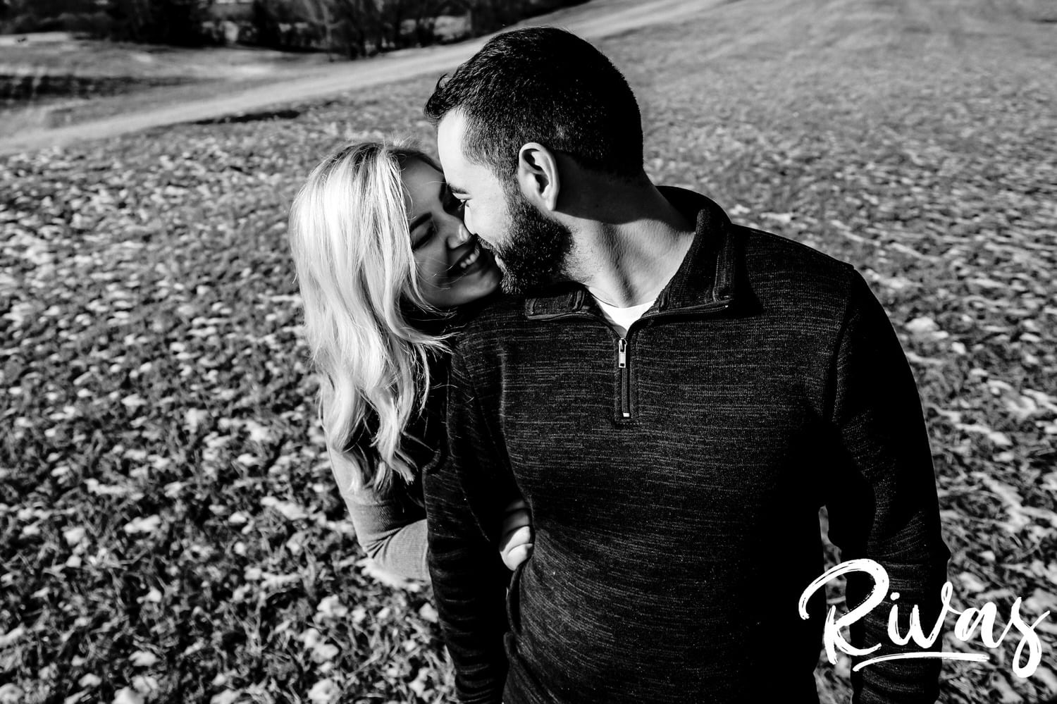 A candid black and white picture of an woman leaning over a man's shoulder to tickle him during their vibrant winter engagement session in Kansas City. 