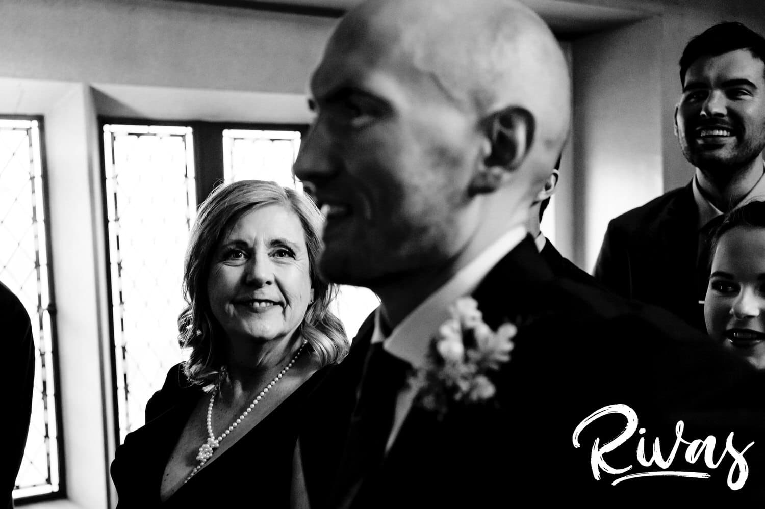 A candid black and white picture taken from behind the groom of his mother looking at him with love moments before walking down the aisle on his sunny winter wedding day. 