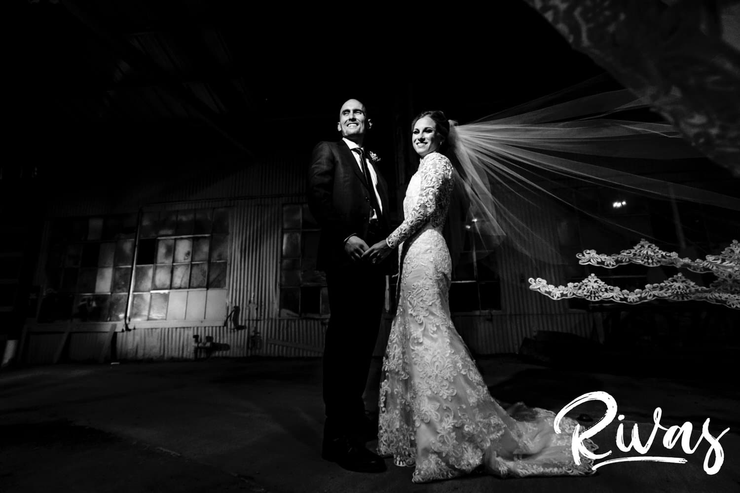 A bold, black and white portrait of a bride and groom holding hands, looking at the camera as the bride's veil blows in the wind on their winter wedding day in Kansas City. 